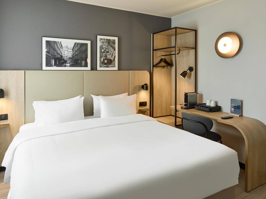 Habitación de hotel con una cama grande, un escritorio con computadora, un espejo y dos cuadros en la pared.