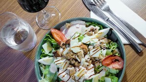 A salad with various ingredients and a glass of red wine on a wooden table. - Campanile PRIME - Paris Pantin (Pantin)