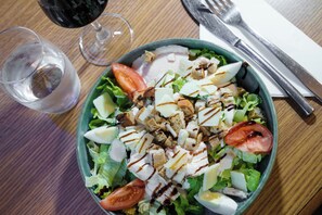 A salad with various ingredients and a glass of red wine on a wooden table. - Campanile PRIME - Paris Pantin (Pantin)