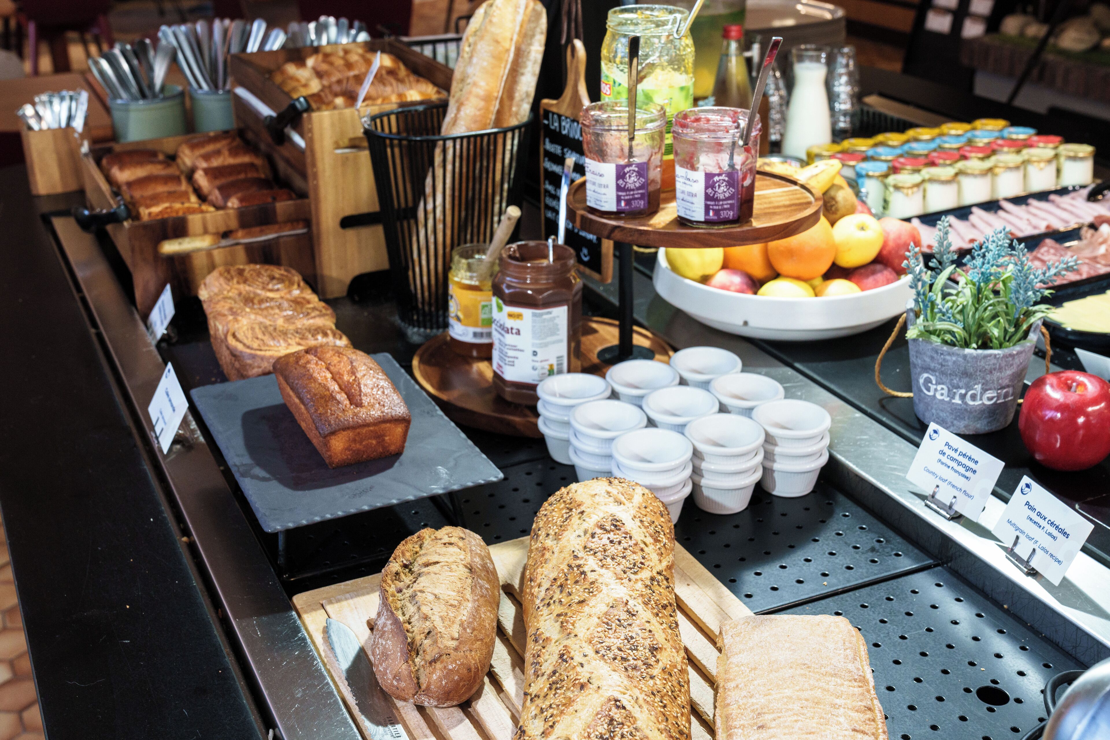 A bakery display with various breads, jars of spreads, and fresh fruits.