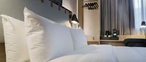 Una cama bien hecha con sábanas blancas, una lámpara de pared y un escritorio de madera con un espejo y un pequeño reloj.
