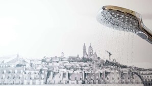 A showerhead with water flowing, set against a blurred cityscape. - Campanile PRIME - Paris Pantin (Pantin)