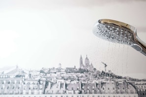 A showerhead with water flowing, set against a blurred cityscape. - Campanile PRIME - Paris Pantin (Pantin)