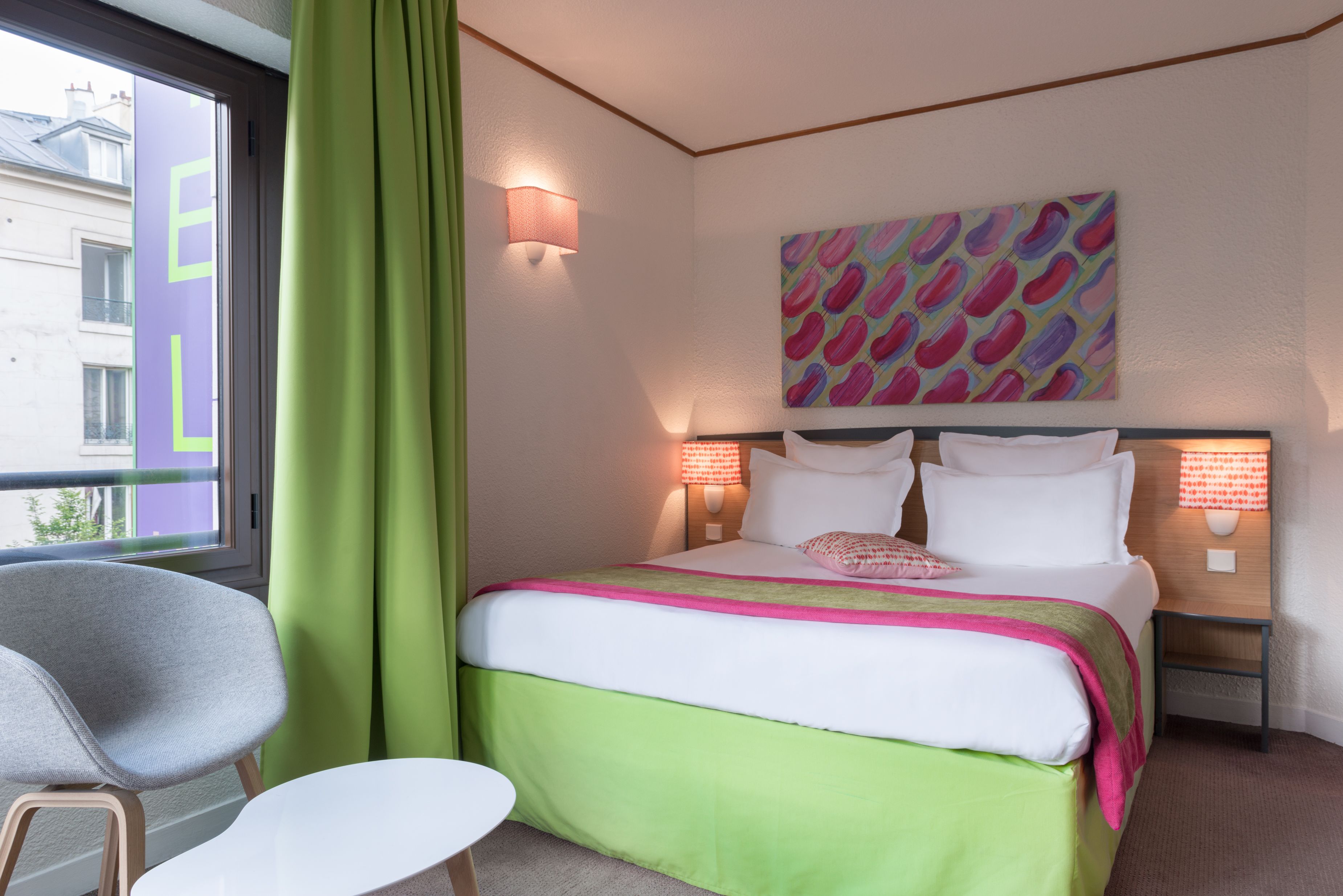 A hotel room with a bed, a chair, a small table, and a window with curtains.
