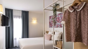 Een hotelkamer met een bed, een televisie, een kledingkast en een plank met schoenen en een mand.