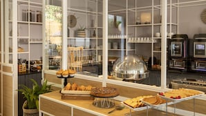 Een buffetgedeelte met diverse gerechten, een koffieapparaat en uitzicht op de keuken via een glazen wand.