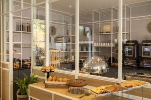 A buffet area with various food items, a coffee machine, and a view of the kitchen through a glass partition.