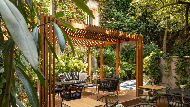 Een terras buiten met een houten pergola, rieten meubilair en een pad van natuursteen.