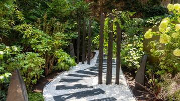 Un sendero en un jardín con guijarros blancos y piedras oscuras, rodeado de abundante vegetación y plantas.