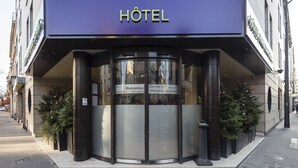 Een hotelingang met een draaideur, een bord met de tekst 'Hôtel' en meertalige welkomstborden.
