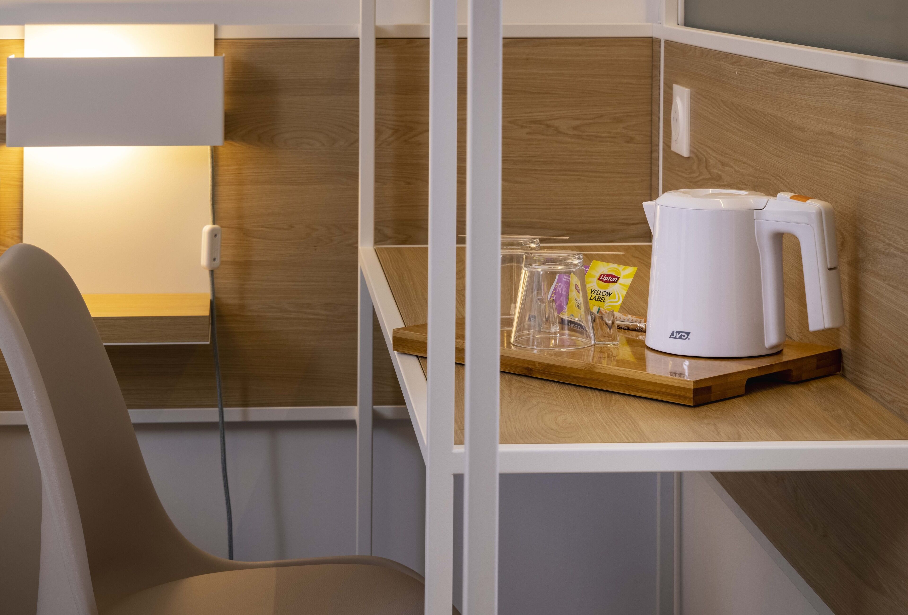 A modern room with a wooden wall, a white chair, a table with a white coffee maker, and a transparent container holding a yellow label.