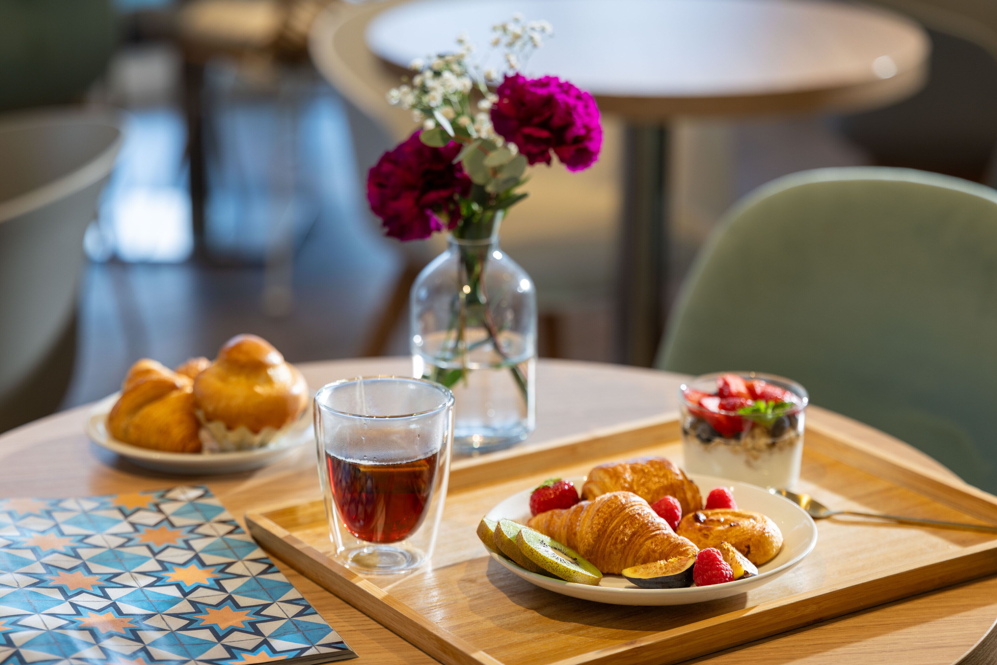 Un desayuno con cruasanes, fresas y una taza de té sobre una bandeja.