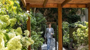 Een houten pergola met een pad dat door weelderig groen en witte bloemen loopt.