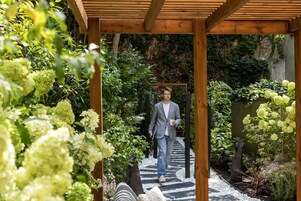 A wooden pergola structure with a pathway leading through lush greenery and white flowers.
