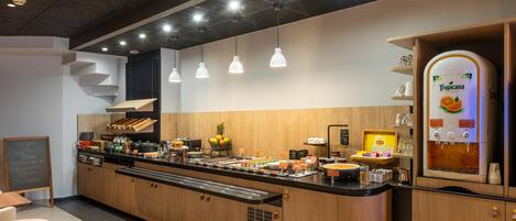 Un buffet pour le petit-déjeuner proposant une variété d’aliments, une présentation de fruits et un distributeur de boissons.