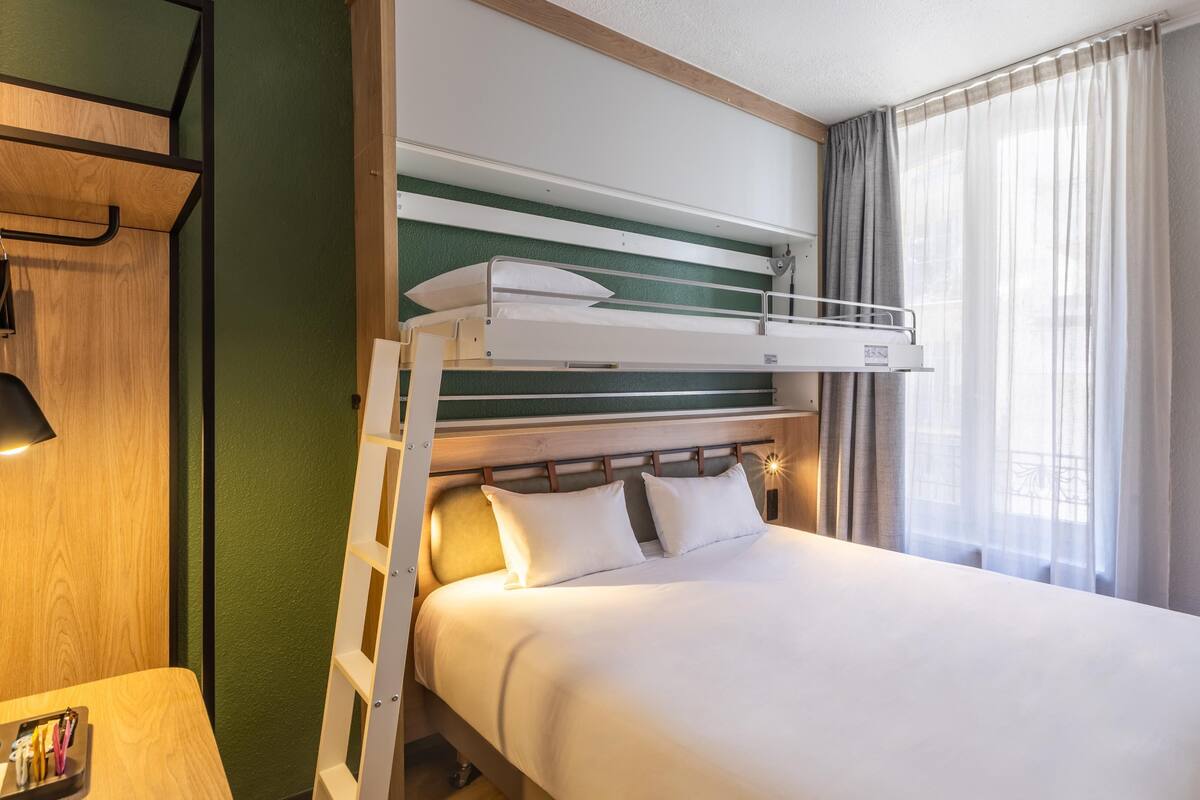 A bunk bed with a ladder, a bedside table with a lamp, a chair, and a large mirror.