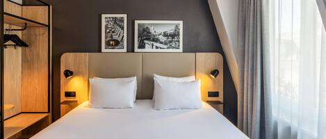 A modern hotel room with a bed, two bedside tables, a wardrobe, and two framed pictures on the wall.