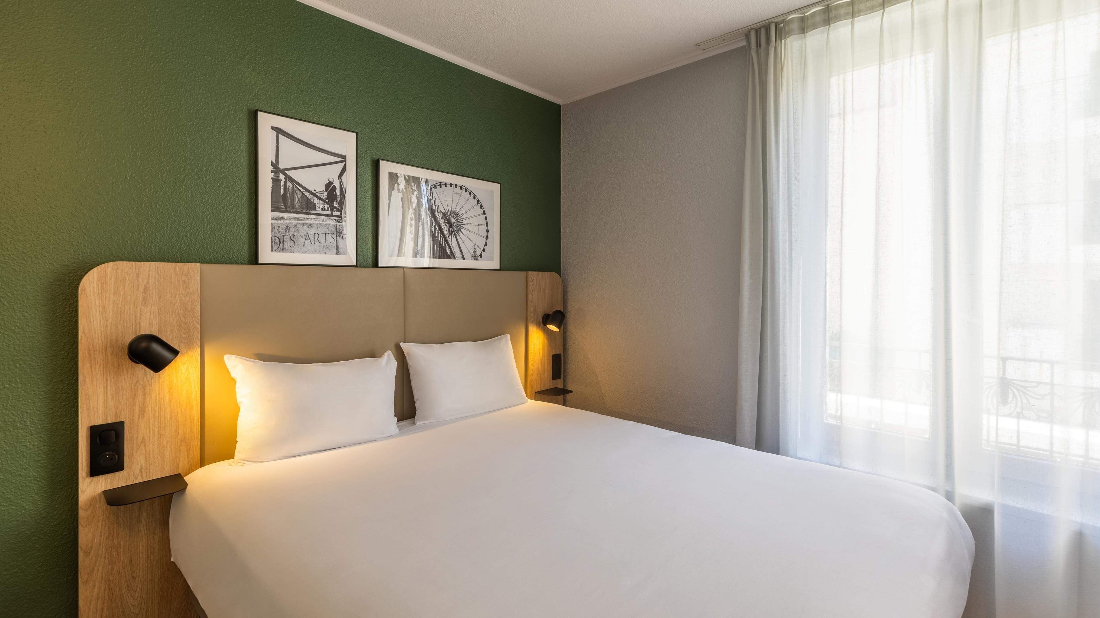 Una habitación de hotel con una cama, dos lámparas de pared y dos cuadros enmarcados.