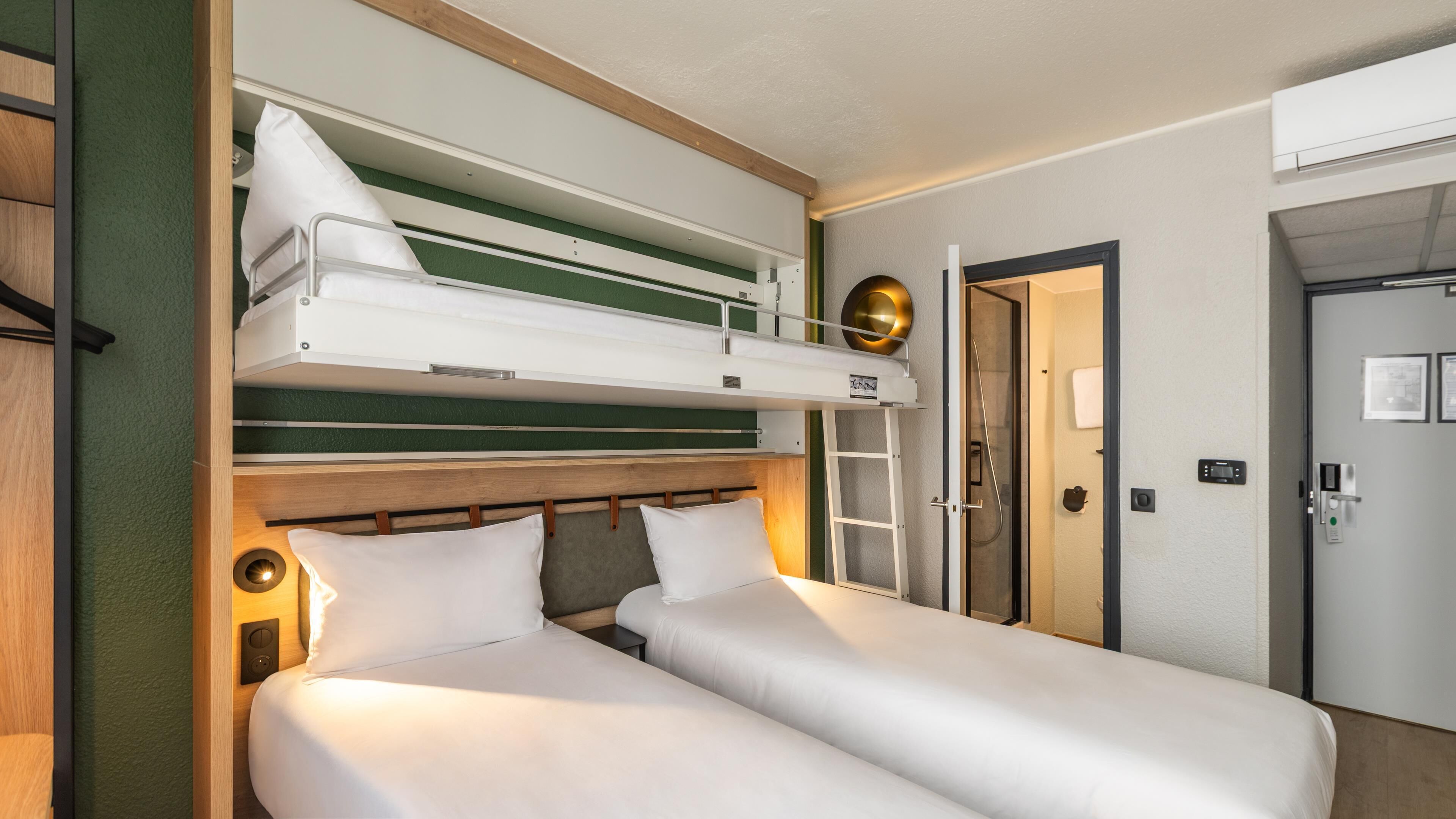 Une chambre d’hôtel équipée d’un lit superposé, d’un lit simple, d’une douche et d’une porte dotée d’une serrure et d’un panneau de commande.