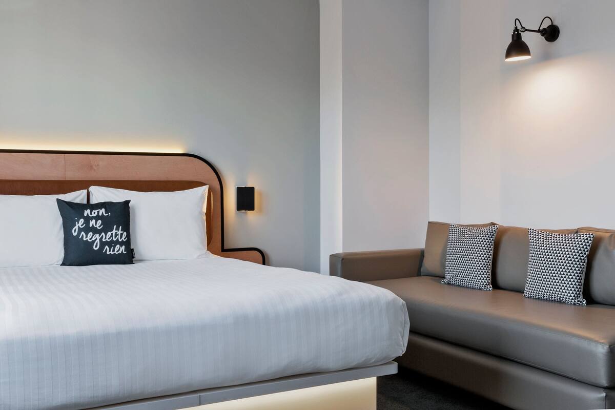 Una habitación de hotel moderna con una cama, un sofá y una lámpara de pared.