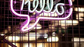 A neon sign with the word "hello" in cursive letters, set against a grid-like background.