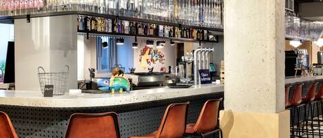 A bar area with a long counter, multiple stools, and a variety of bottles and glasses on shelves.