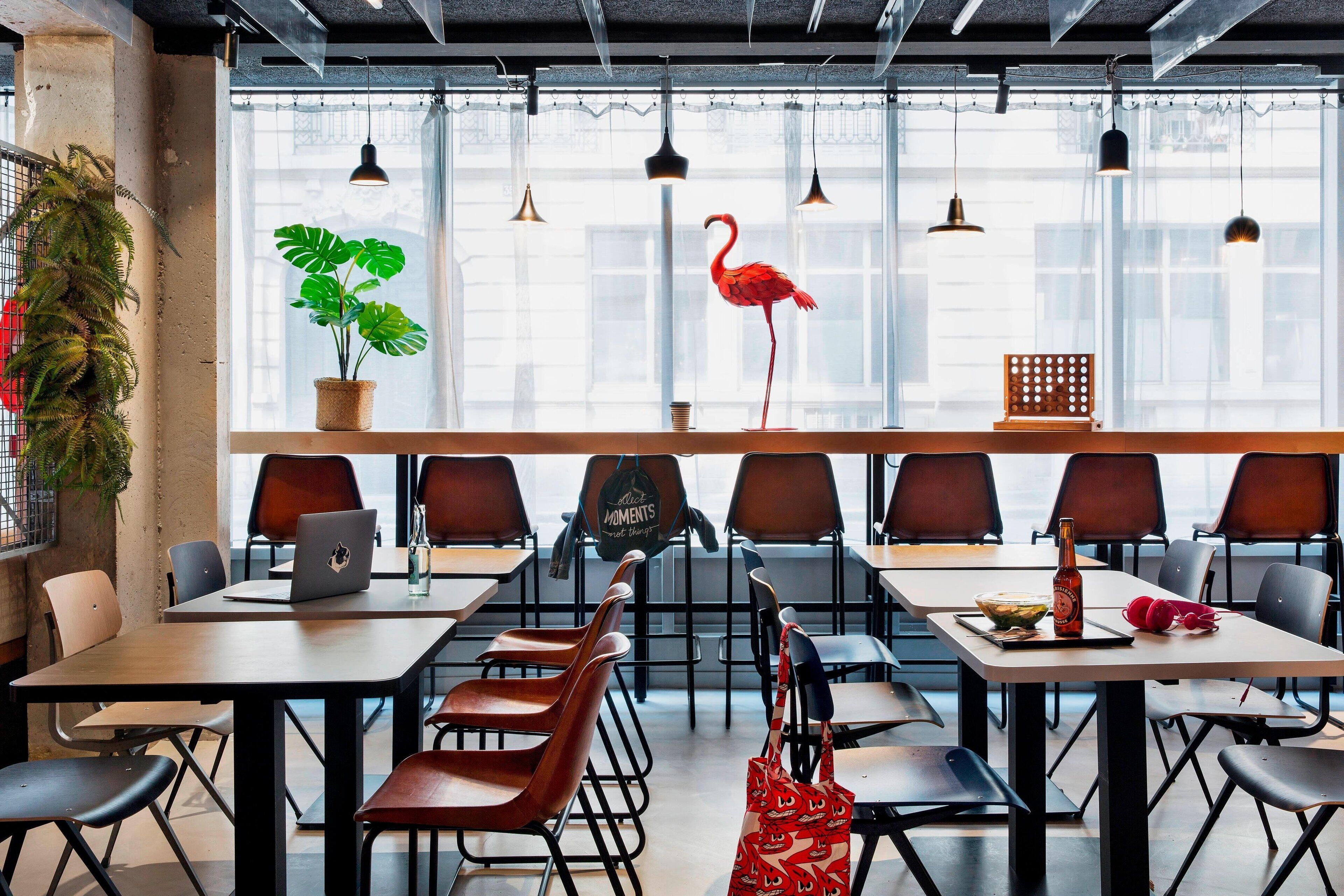 A modern office space with a long table, chairs, a laptop, a potted plant, and a decorative flamingo.