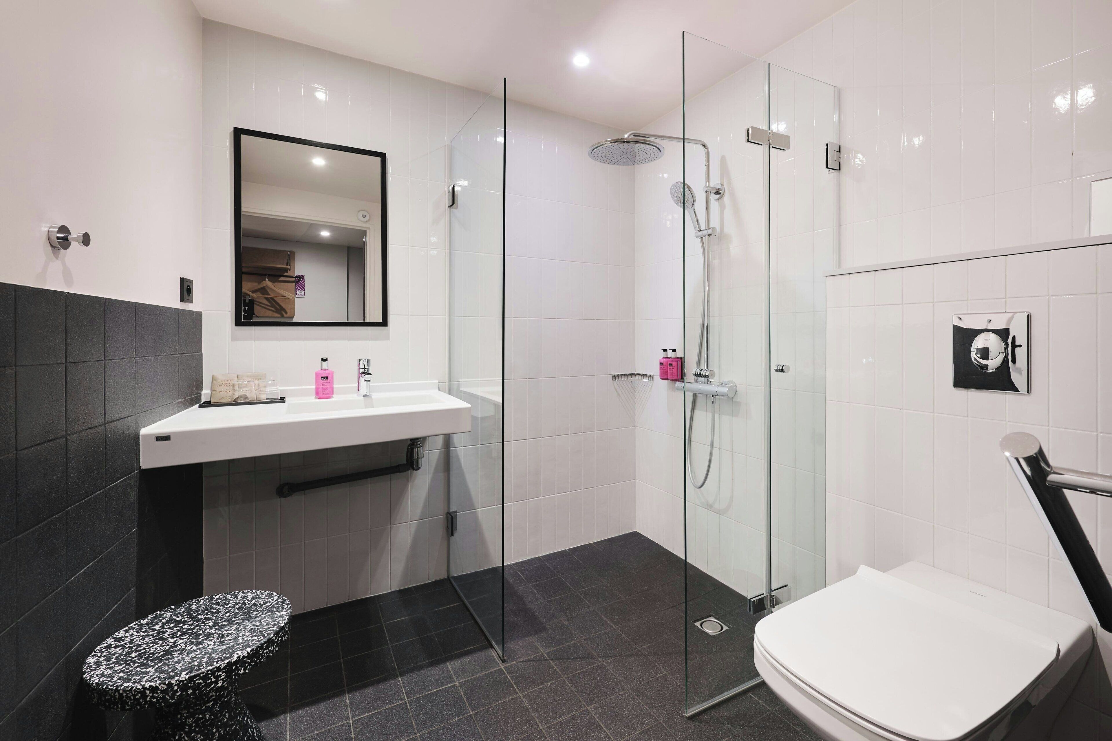 A modern bathroom with a glass shower enclosure, a white sink with a mirror above it, and a black tiled floor.