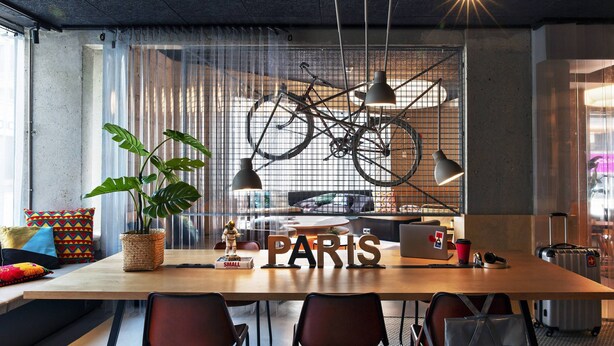 A modern workspace with a large table, chairs, a bicycle, and a "PARIS" sign. - Moxy Paris Bastille France (Paris)
