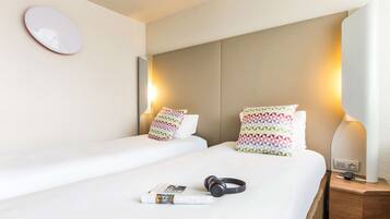 Une chambre d’hôtel avec un lit, des oreillers, une table de chevet avec une lampe et une paire d’écouteurs posés sur le lit.