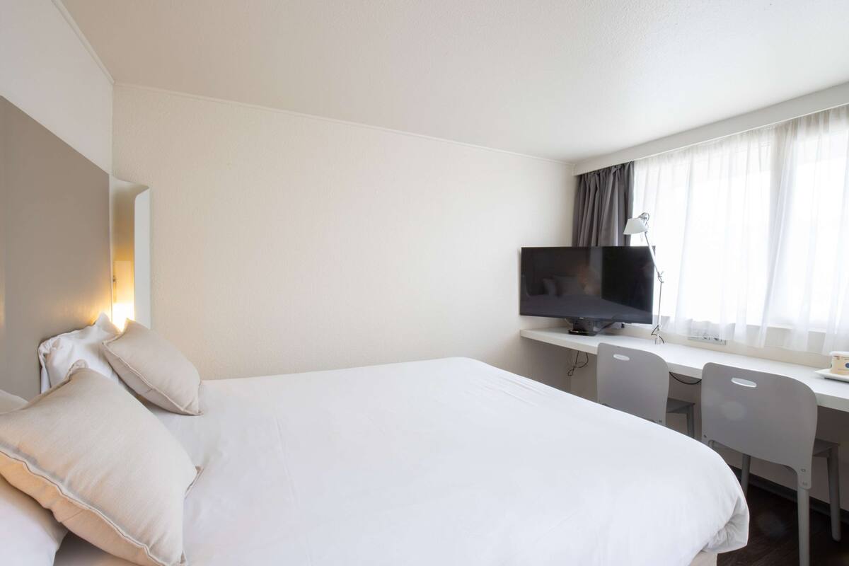 A hotel room with a large bed, a desk with a computer, and a TV.