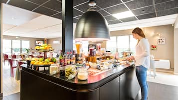A buffet area with a variety of food items and beverages, a large pendant light, and a woman preparing food.