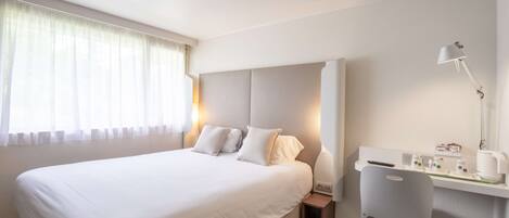 Una habitación de hotel con una cama grande, un escritorio con silla, una lámpara y una mesita de noche.