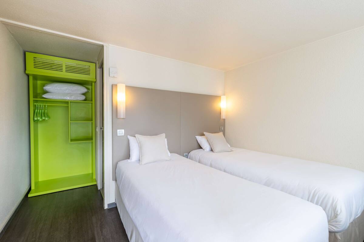 A hotel room with two single beds, a green wardrobe, and two wall-mounted lights.