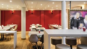 Un comedor moderno con mesas blancas, paredes rojas y un cuadro en la pared.