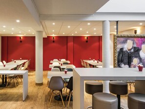 Un espace repas moderne avec des tables blanches, des murs rouges et un tableau accroché au mur.