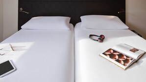 Una cama doble con sábanas blancas, un par de gafas, un teléfono inteligente y una revista a la izquierda.