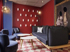Un salón moderno con una pared roja, diversas opciones de asiento que incluyen un sofá y sillones, piso estampado y una lámpara decorativa.