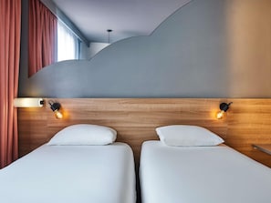 A hotel room with two beds, wooden headboard, and wall-mounted light fixtures.