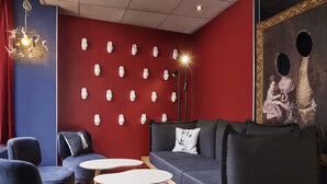 Un salón moderno con una pared roja, diversas opciones de asiento que incluyen un sofá y sillones, piso estampado y una lámpara decorativa.