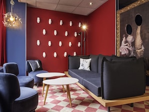 Un salon moderne avec un mur rouge, plusieurs options d’assises, notamment un canapé et des fauteuils, un sol à motifs et un luminaire décoratif.