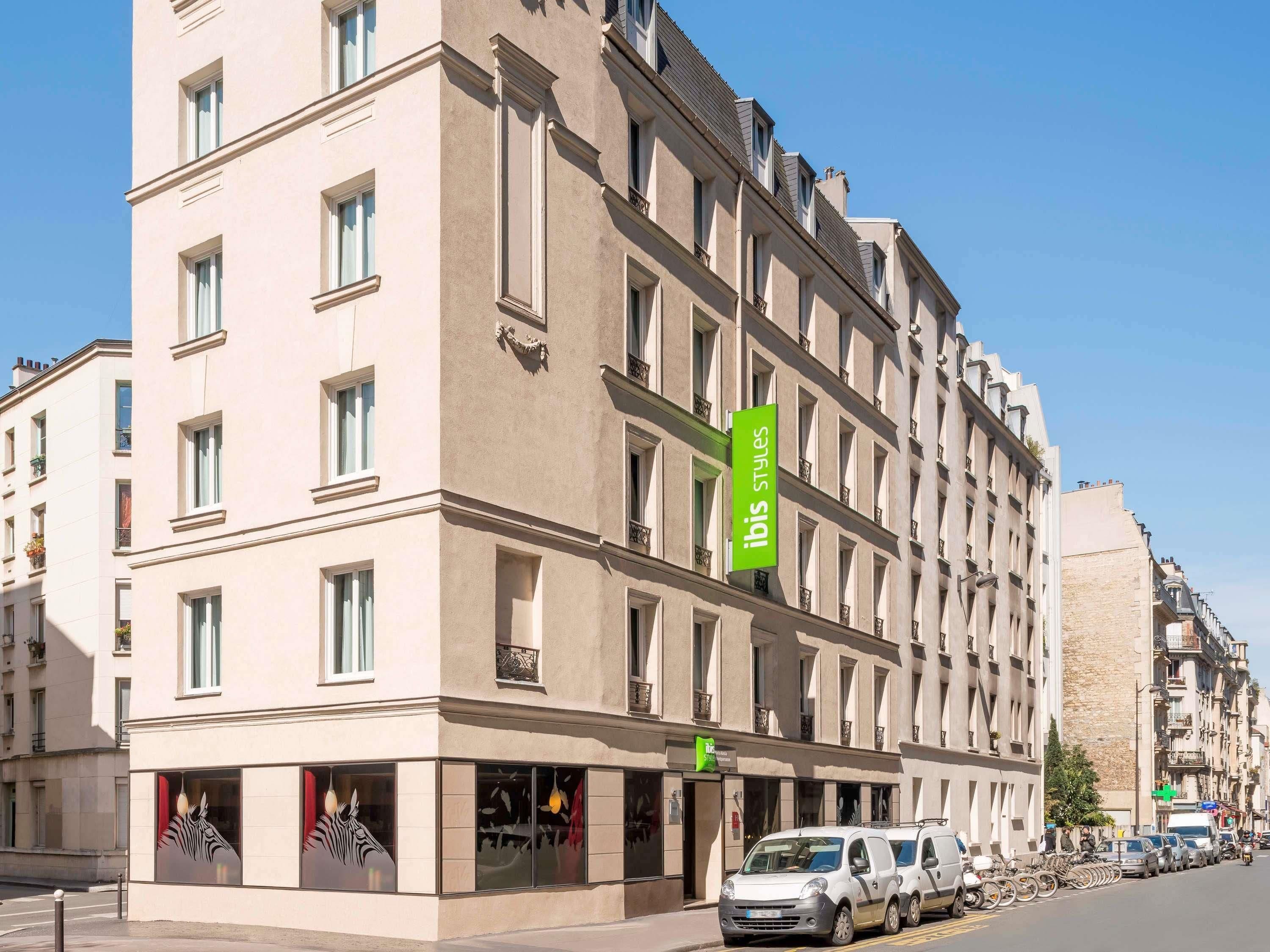A multi-story hotel building with a green sign indicating 'Ibis Styles' on the facade.
