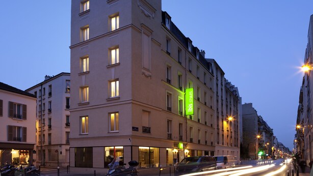 Un hotel de varios pisos con señalización iluminada, un restaurante en la planta baja y vistas a la calle con vehículos estacionados.
