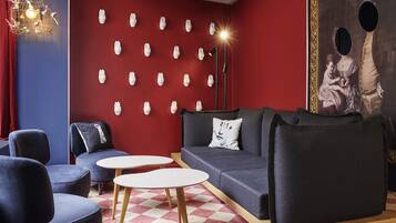 Un salón moderno con una pared roja, diversas opciones de asiento que incluyen un sofá y sillones, piso estampado y una lámpara decorativa.