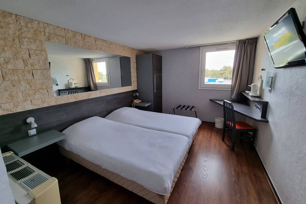 Ein Hotelzimmer mit einem Bett, einem Schreibtisch, einem Sessel, einem Fernseher, einem Spiegel und einem Fenster.
