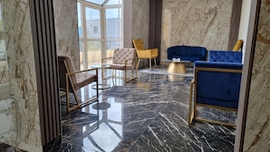 Un vestíbulo moderno con suelo de mármol, un separador de vidrio y una zona de estar con un sofá azul y dos sillones.