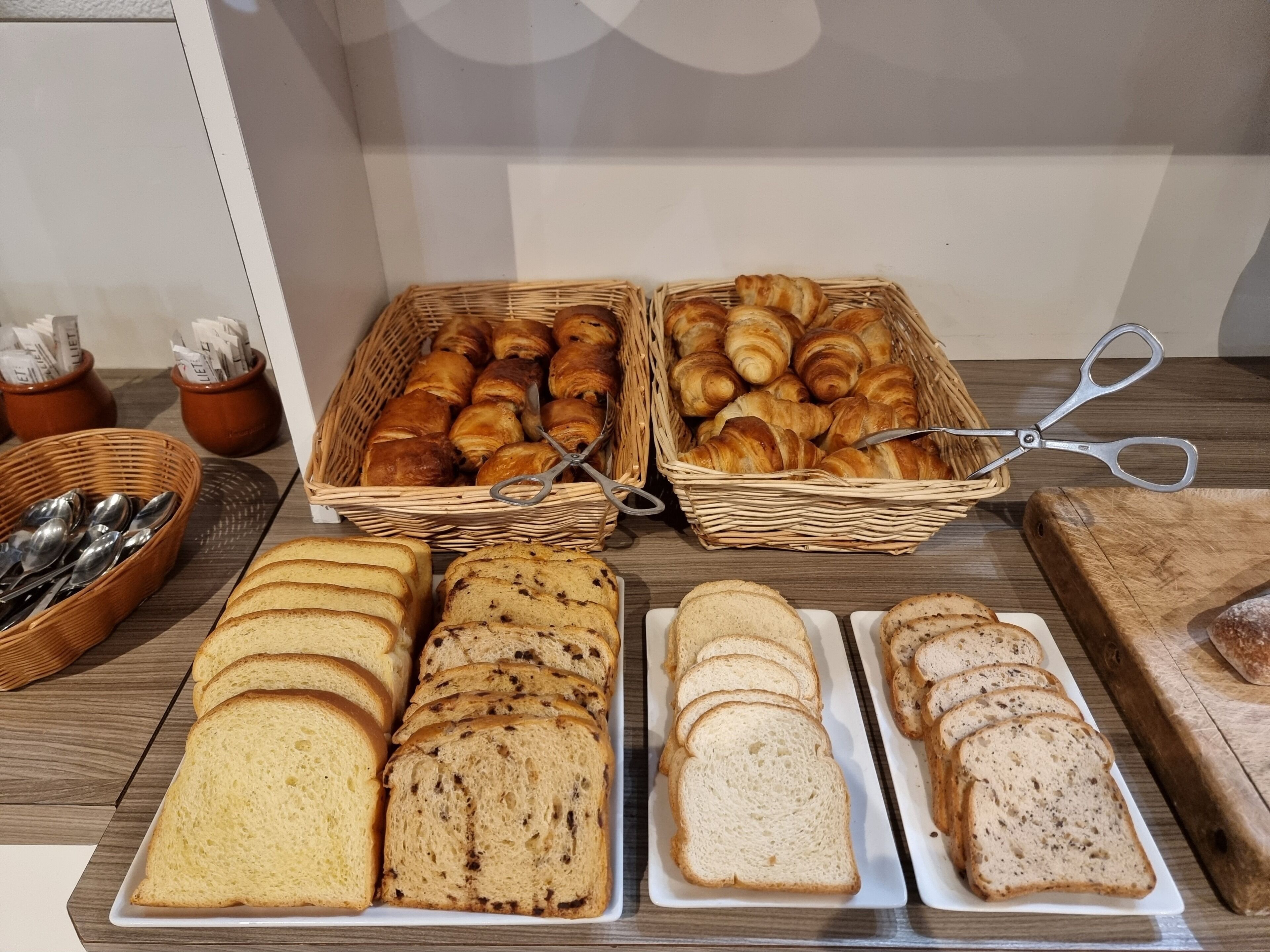A buffet with bread, pastries, and utensils.
