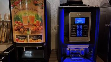 A self-service beverage dispenser and a coffee machine with a digital interface, both placed on a counter with a textured wall in the background.