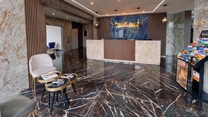 Un moderno vestíbulo de hotel con un mostrador de recepción de mármol, una zona de estar con un atril para revistas y una exposición de folletos.