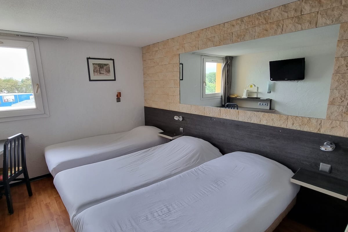 Ein Hotelzimmer mit zwei Betten, Holzboden, Fenster, Spiegel, Fernseher und einem kleinen Tisch.